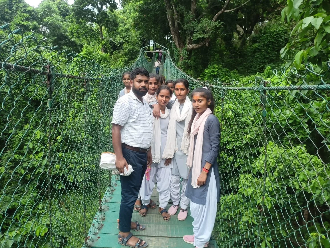Students and a teacher together on a suspension bridge in a green landscape
